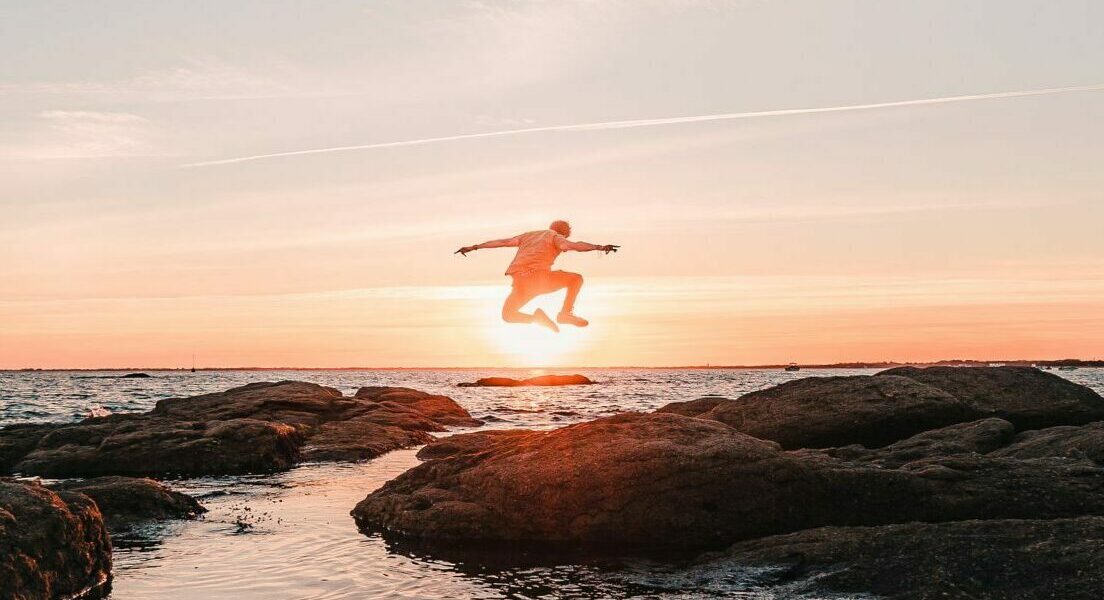 Homme sautant sur les rochers au milieu de l'eau de Pointe de Mousterlin au coucher de soleil