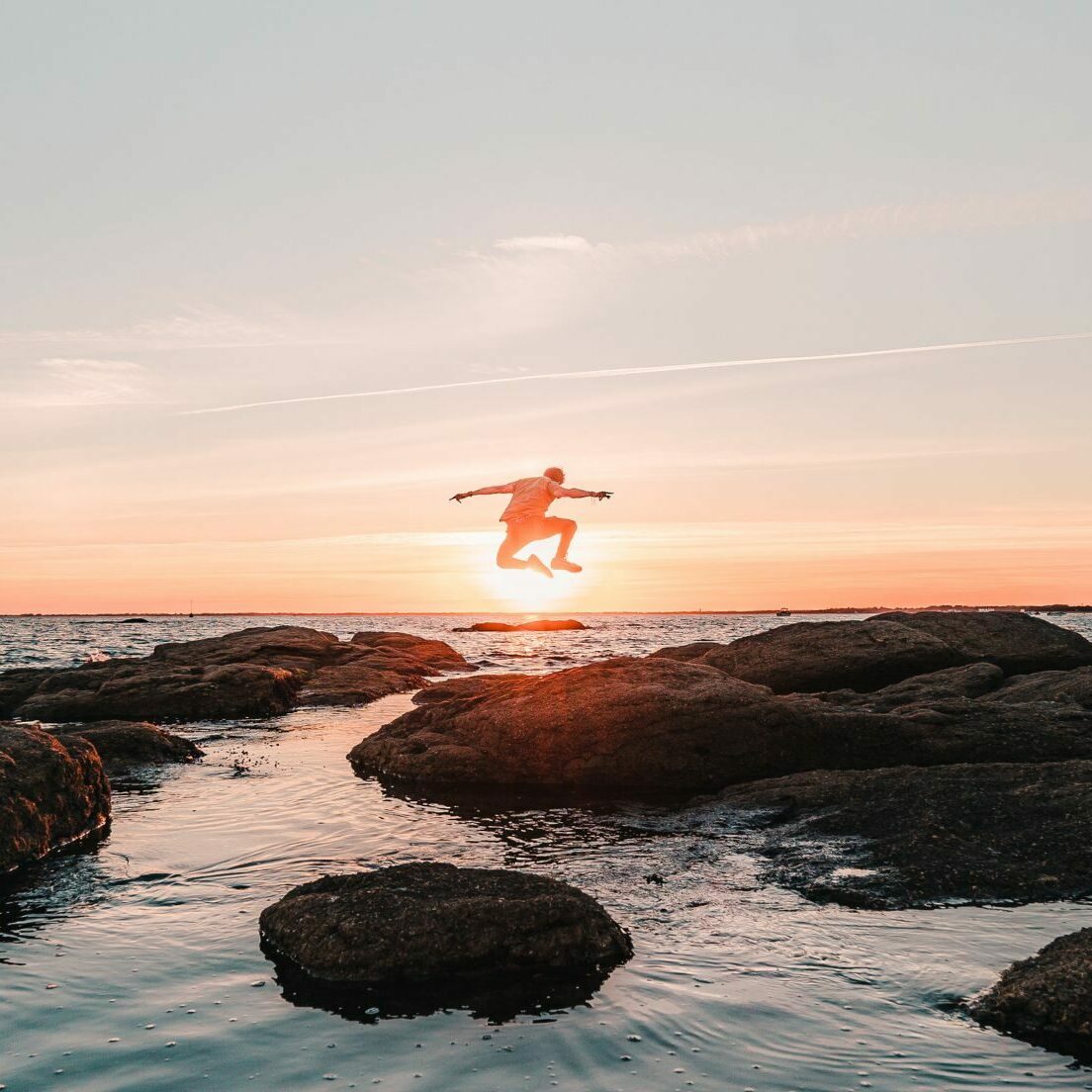Homme sautant sur les rochers au milieu de l'eau de Pointe de Mousterlin au coucher de soleil